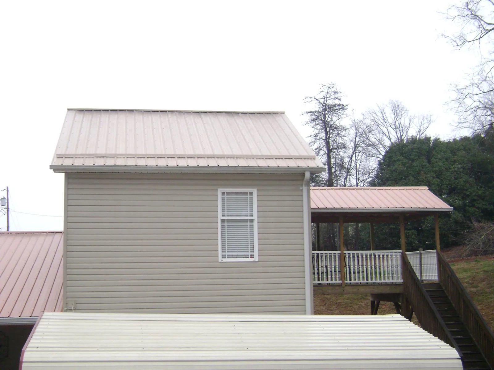 Tan metal roofs on a two story addition and attached porch, from a Roof Replacement job in Sidney
